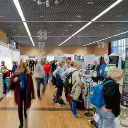 Mehrere Personen gehen durch eine Halle über die Ausstellermesse der chor.com und stehen an Ständen.